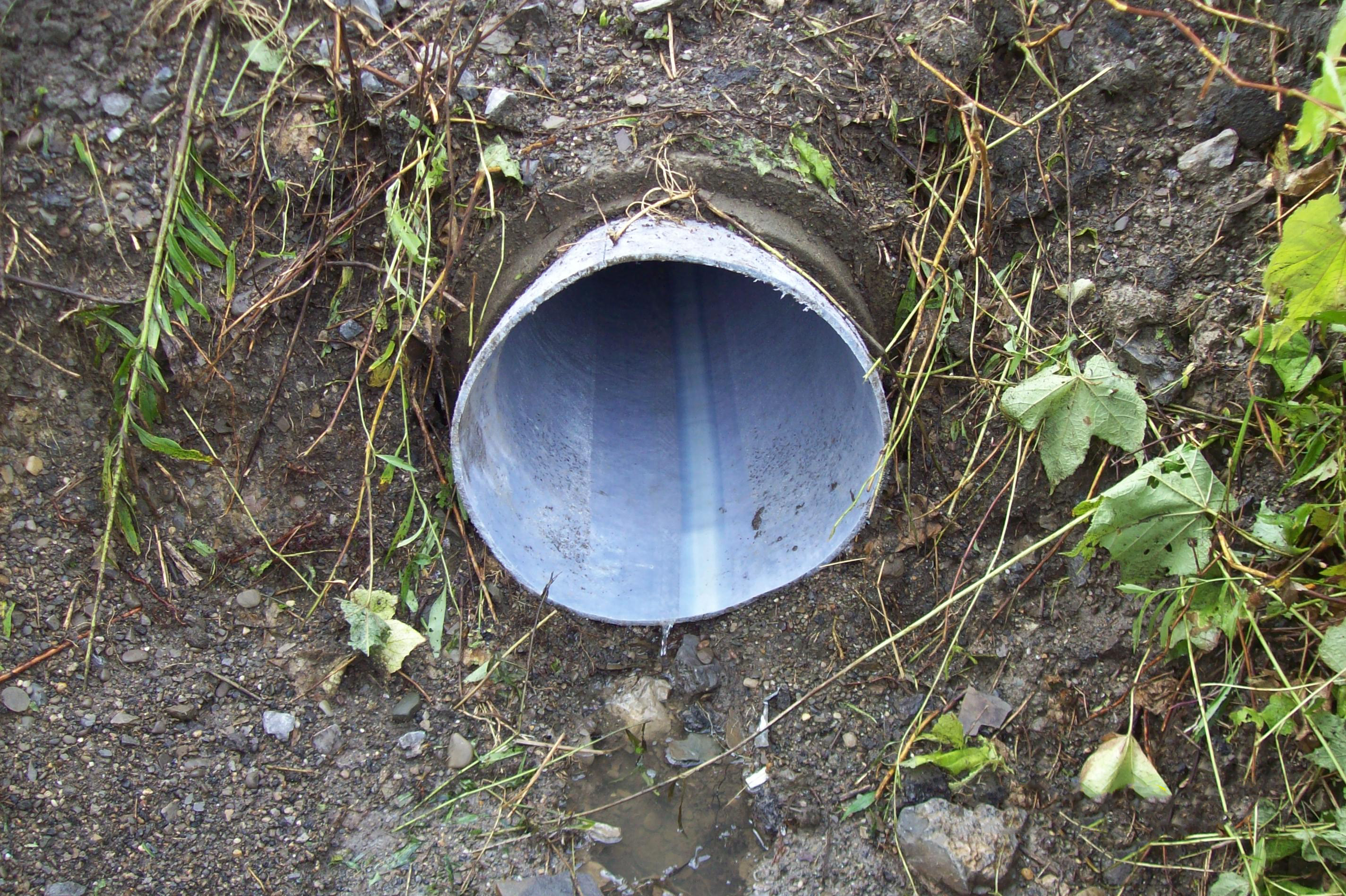 An image of a finished pipe outlet coming out of  the ground with water flowing out of the pipe.
